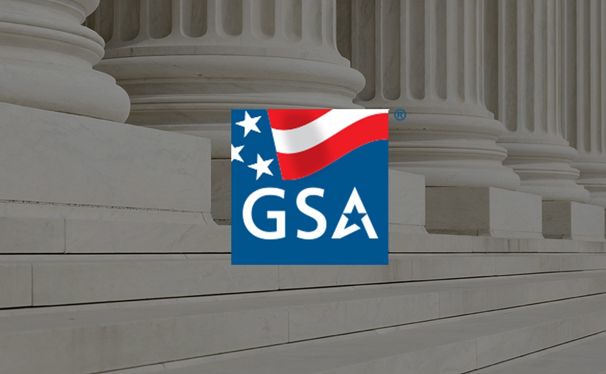 The logo features a blue square with a stylized American flag in the top left corner, showing three white stars on a blue background and a red and white wavy stripe. Below the flag, the letters "GSA" are prominently displayed in white, with the "A" incorporating a star design. The background shows large white marble columns and steps, suggesting a government building.